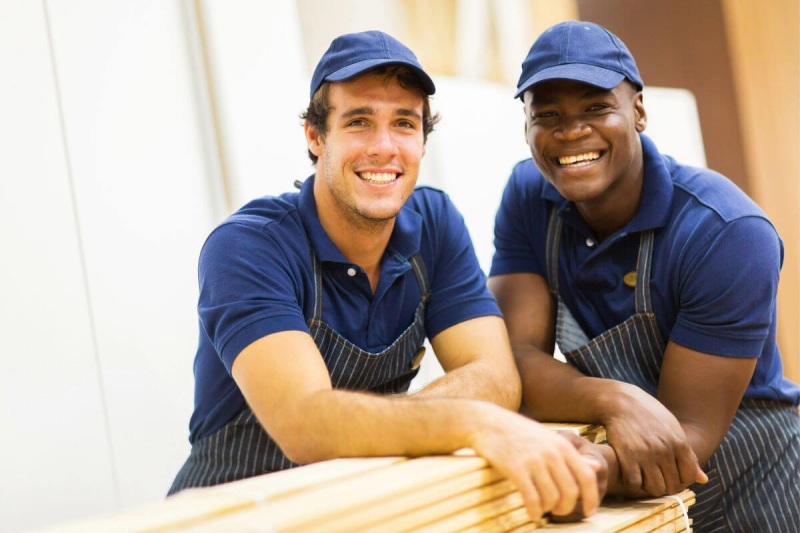 Two men in blue shirts and hats are smiling.